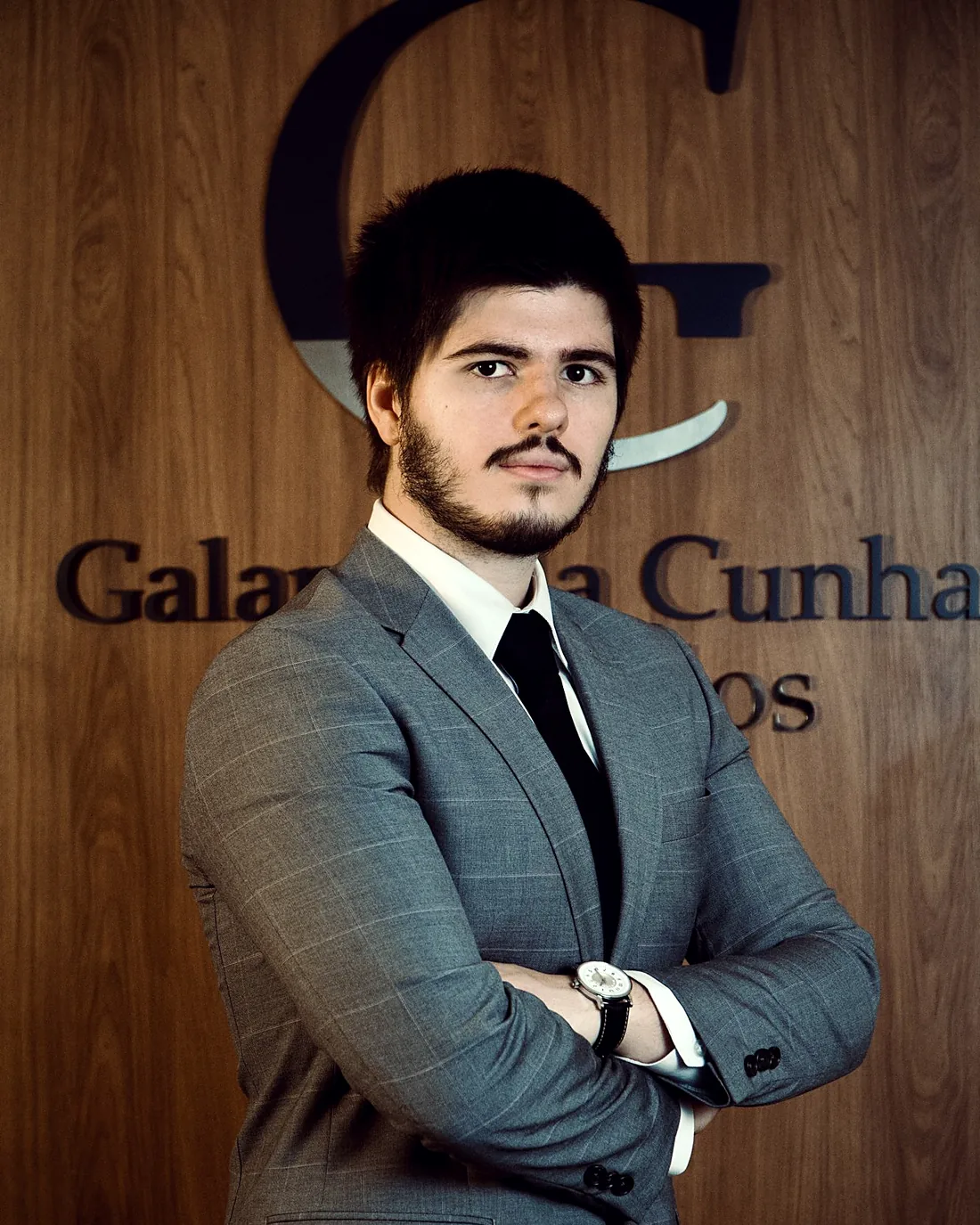 Arthur Galante da Cunha, de braços cruzados, em frente à parede de madeira com a marca do escritório