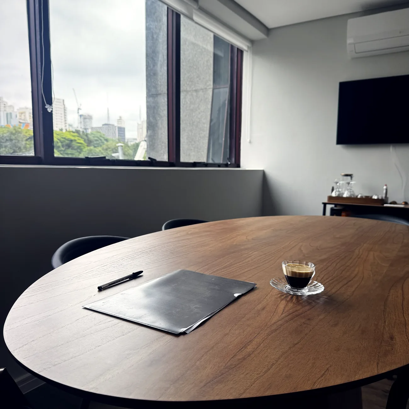 Sala de reuniões do escritório, com mesa de madeira, café servido e vista da cidade